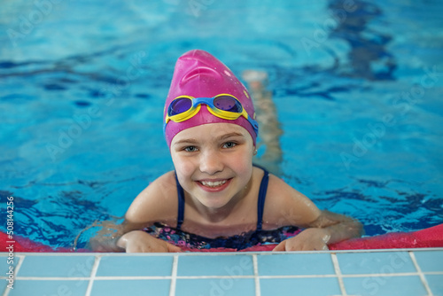 Happy child girl swims in swimming pool. Swim cap and goggles. Training and sports concept.