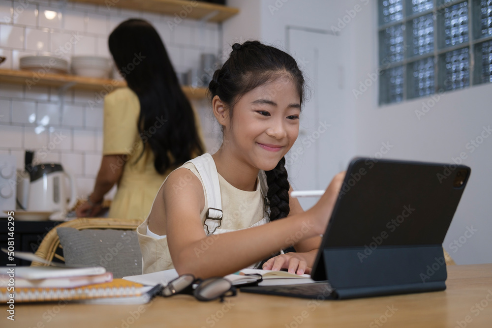 Happy girl studying virtual remote lesson on video call with computer tablet in home kitchen. Happy girl studying virtual remote lesson on video call with computer tablet in home kitchen.