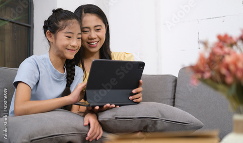 Asian mother and her sweet little daughter using digital tablet together on sofa at home, Weekend family leisure.