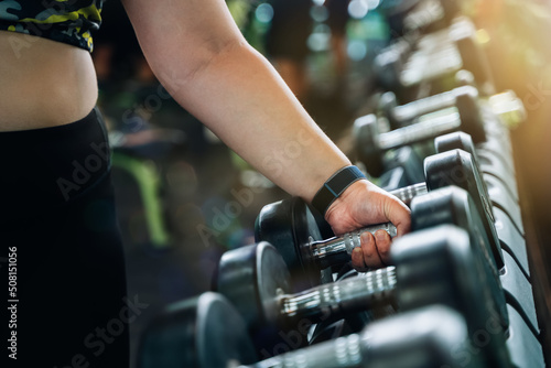 Overweight woman hand takes dumbbells in gym closeup. Athletic woman lifting dumbbell weights for exercise in fitness.
