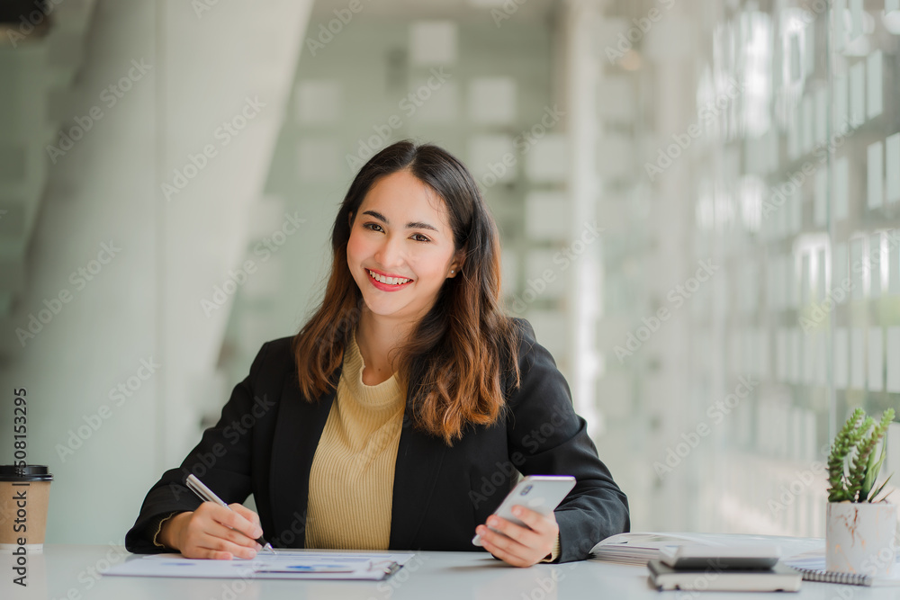 Asian businesswoman or accountant working with laptop and mobile phone. Smile and be happy while sitting at your desk with your financial documents. modern office calculator Asian businesswoman or accountant working with laptop and mobile phone. Smile and be happy while sitting at your desk with your financial documents. modern office calculator