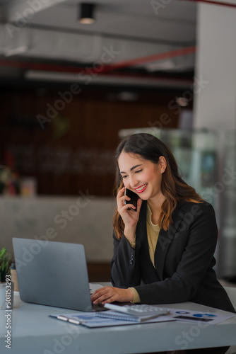 Asian businesswoman or accountant working with laptop and mobile phone. Smile and be happy while sitting at your desk with your financial documents. Vertical modern shape office calculator