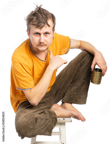 dirty shaggy, bankrupt in a torn t-shirt and brown jeans, barefoot. the thief sits with his legs tucked under him. the bum looks insolently, threatens us, putting his finger to his throat like a knife photo