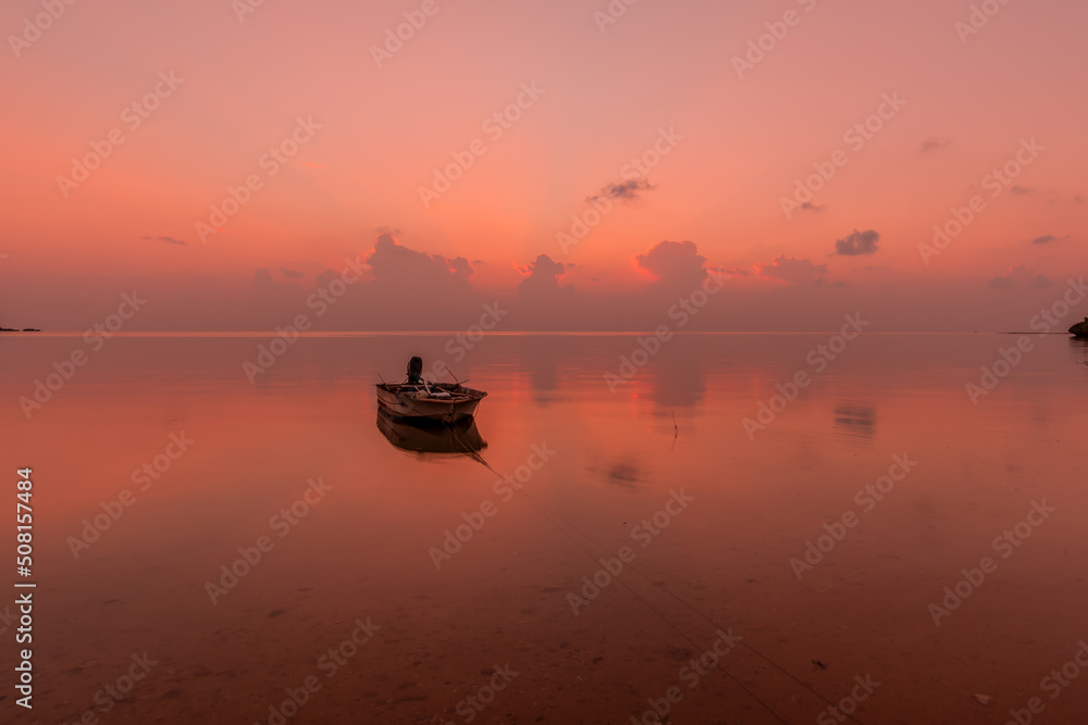 Boat floating on a smooth pink ocean at dusk.