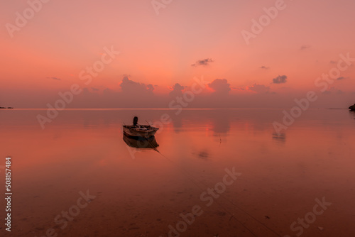 Boat floating on a smooth pink ocean at dusk.