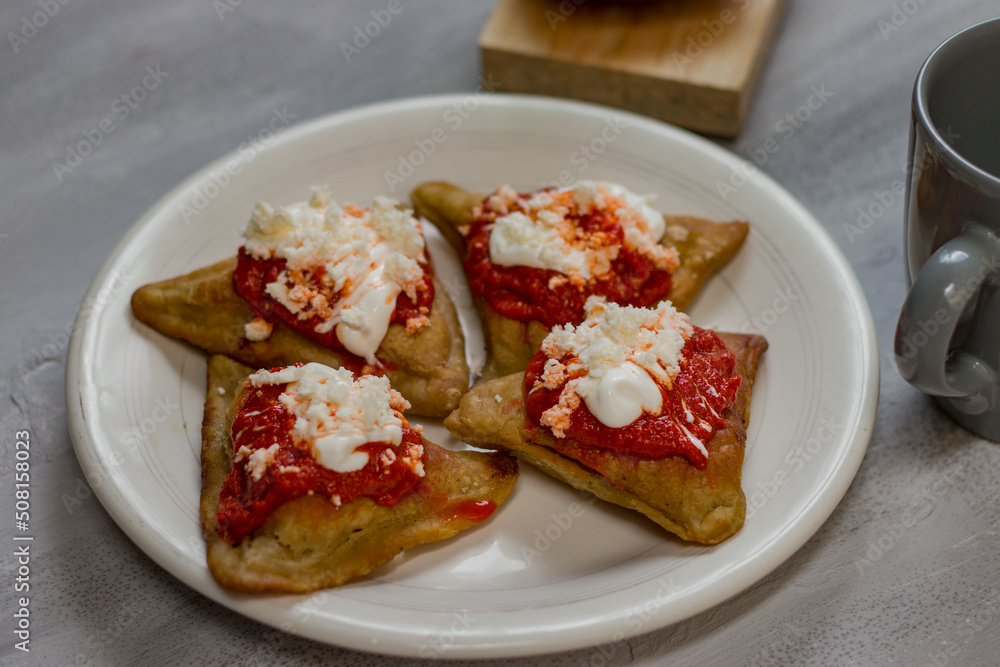 Rich, healthy breakfast of four salty dough empanadas, stuffed with beans, with tomato sauce, cream and cheese. Rich, healthy breakfast of four salty dough empanadas, stuffed with beans, with tomato sauce, cream and cheese.