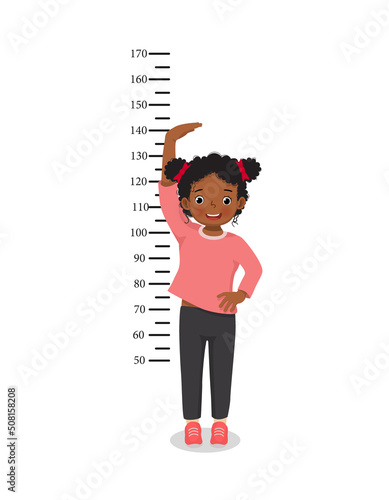 Cute Little African girl measuring height of her growth on the background of wall 