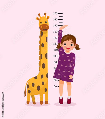 Cute Little girl measuring height of her growth on the background of wall with giraffe