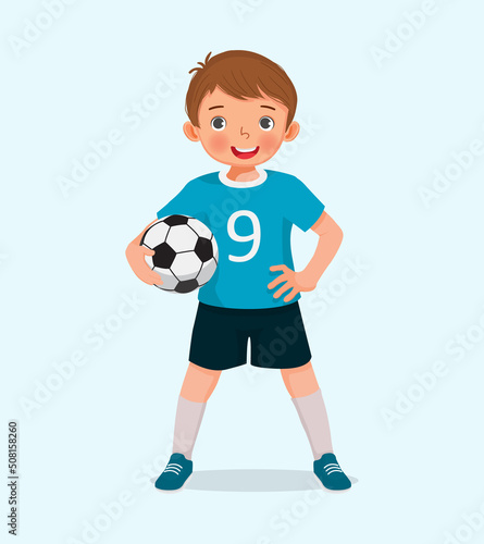 Portrait of cute little boy in sportswear holding a soccer ball posing with hand on the waist