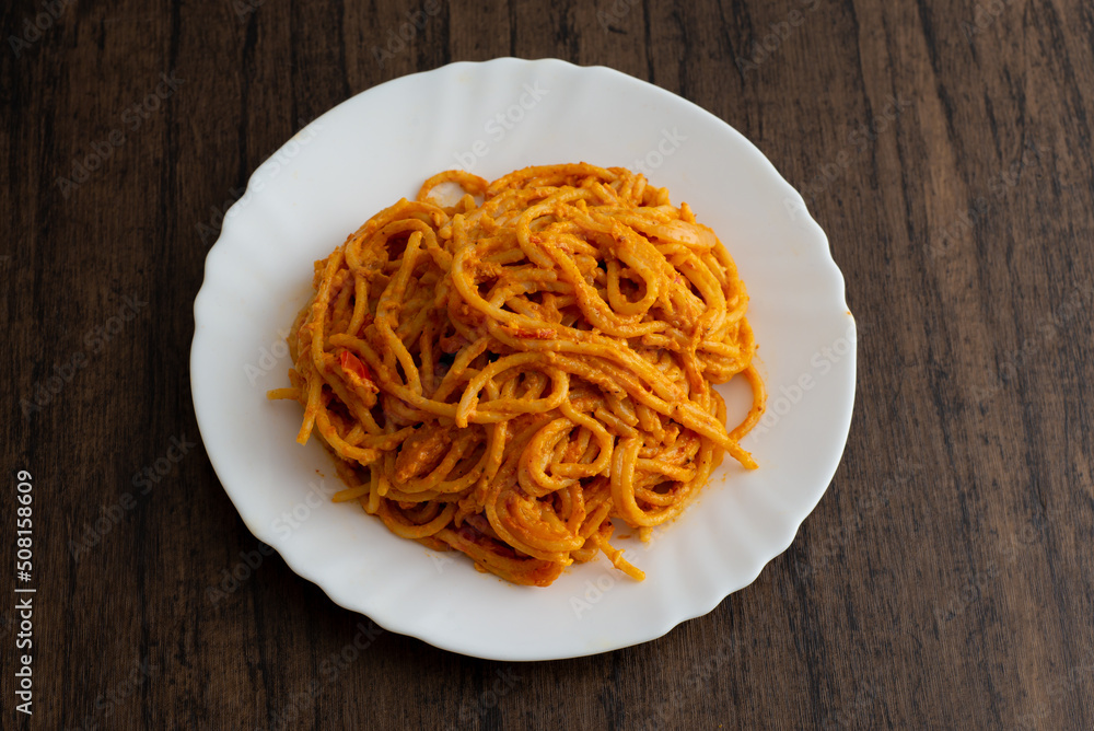 Spaghetti dish served in white plate on wooden table.