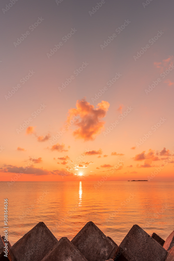 Morning sun in orange and pink shades rising at sea horizon, colorful clouds, rocks.
