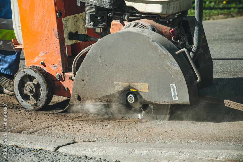 Portable asphalt cutter close-up, cuts asphalt with a diamond blade to repair part of the roadway. Cutting road works with a gasoline-powered angle grinder. Repair of asphalt roads. Portable asphalt cutter close-up, cuts asphalt with a diamond blade to repair part of the roadway. Cutting road works with a gasoline-powered angle grinder. Repair of asphalt roads.
