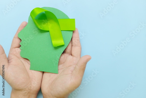 Obraz na płótnie Hand holding human head profile with lime green awareness ribbon on brain. Lyme disease, psychosis, childhood mental illness, lymphoma and postpartum depression care concept. w salonie