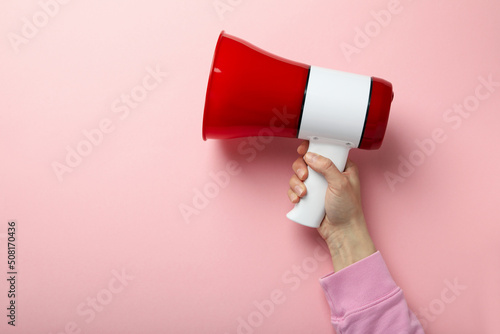 Female hand with megaphone on pink background