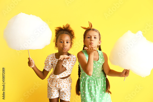 Cute little girls with cotton candy on yellow background