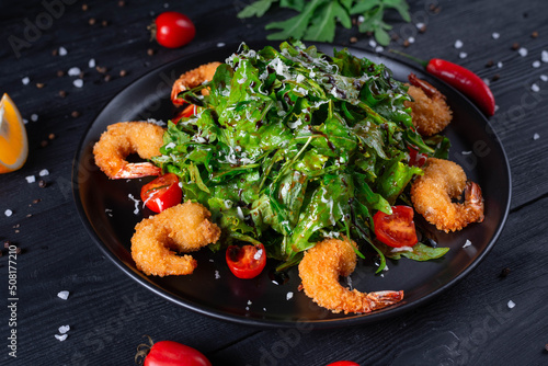 salad of fried shrimp, arugula leaves and tomatoes on a black wooden background
