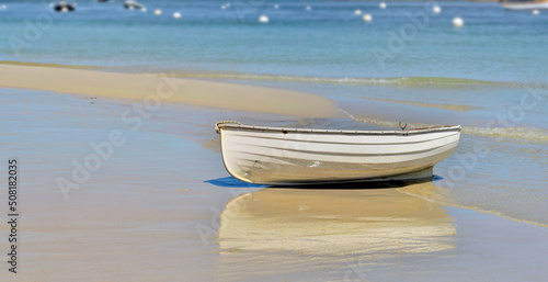 white boat placed on the sand near the blue sea with reflection on the wet sand