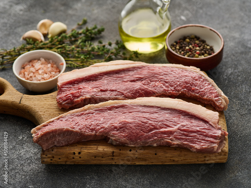 Photo Picanha raw organic  beef steaks with seasoning over rustic dark background