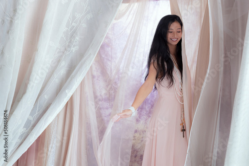 A beautiful Asian woman wearing a pink vintage dress and surrounded by soft, draped fabric