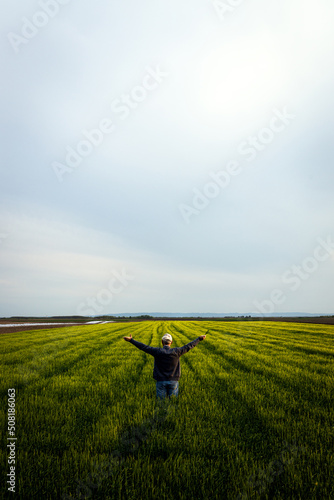 Rear view of senior farmer standing in barley field with his outstretched arms at sunset.