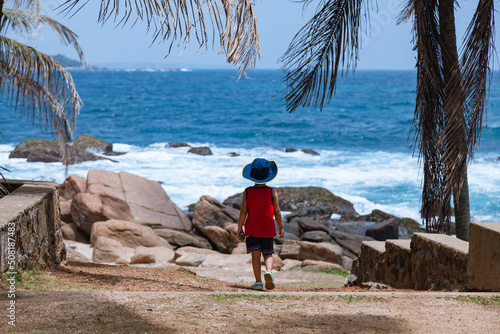 Obraz na płótnie Little boy walking to a beautiful blue ocean with a hat w salonie