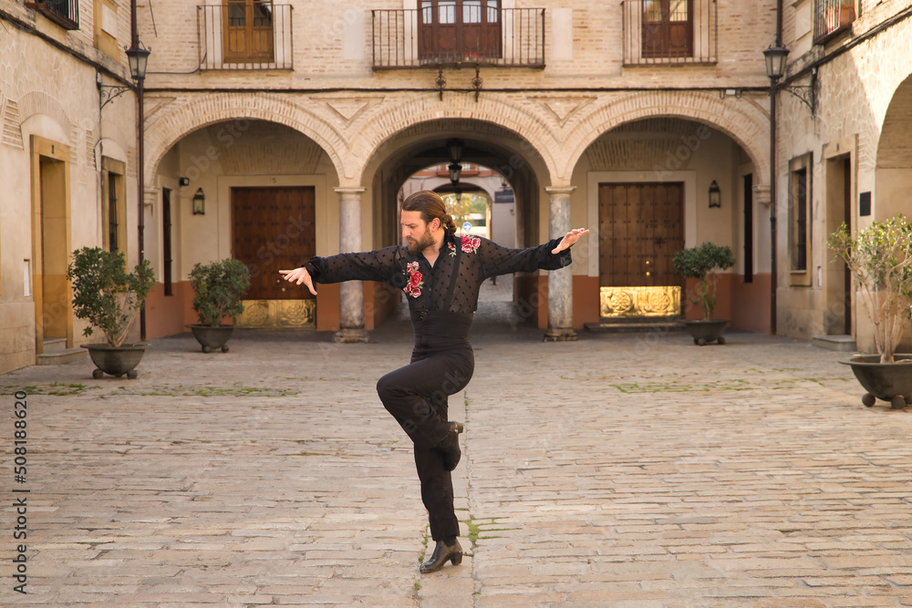 Young man with beard and ponytail, wearing black transparent shirt with black polka dots and red roses, black pants and jacket, dancing flamenco in the city. Concept art, dance, culture, tradition.