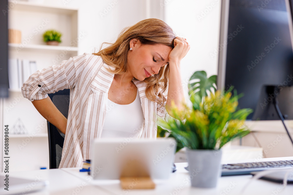 Woman having backpain and headache while sitting at her desk in an office Woman having backpain and headache while sitting at her desk in an office