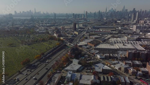 Aerial panoramic shot of large city. Busy multilane expressway leading along cemetery. Downtown skyscrapers in distance. Queens, New York City, USA photo