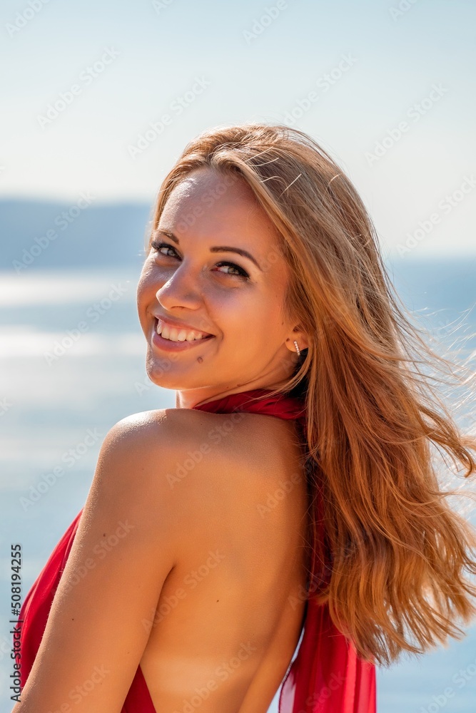 Smiling young woman in a red dress looks at the camera. A beautiful tanned girl enjoys her summer holidays at the sea. Portrait of a stylish carefree woman laughing at the ocean. Smiling young woman in a red dress looks at the camera. A beautiful tanned girl enjoys her summer holidays at the sea. Portrait of a stylish carefree woman laughing at the ocean.