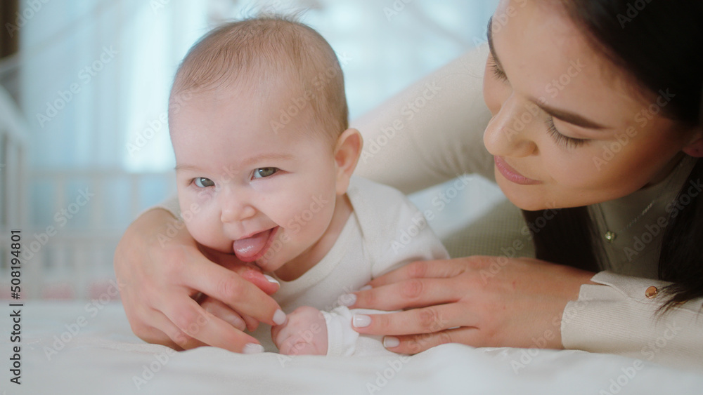 In the bedroom in front of the camera amazing young mother with a large smile hugging lovely the baby girl and looking straight to the camera In the bedroom in front of the camera amazing young mother with a large smile hugging lovely the baby girl and looking straight to the camera