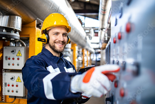 Fényképezés Smart caucasian factory worker wearing hardhat, earmuffs and working in power plant