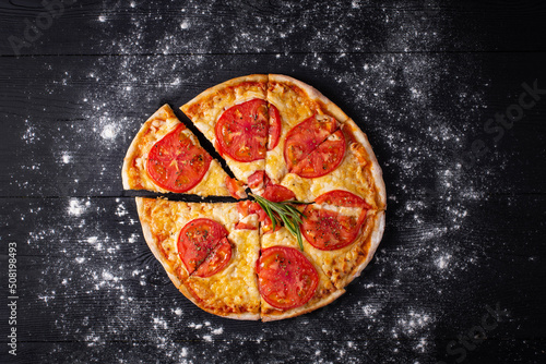 pizza margarita, around flour on a black wooden background