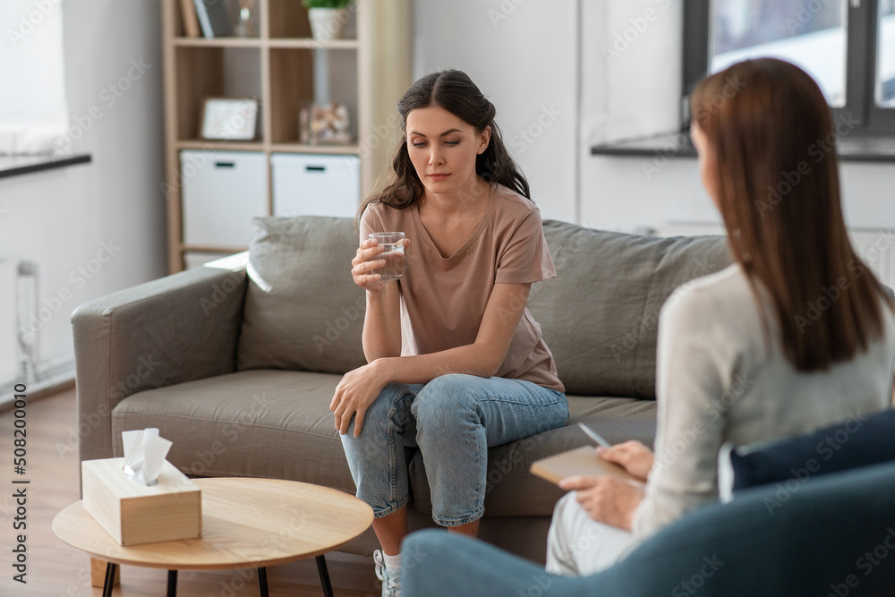 psychology, mental health and people concept - sad young woman patient with glass of water and woman psychologist at psychotherapy session psychology, mental health and people concept - sad young woman patient with glass of water and woman psychologist at psychotherapy session