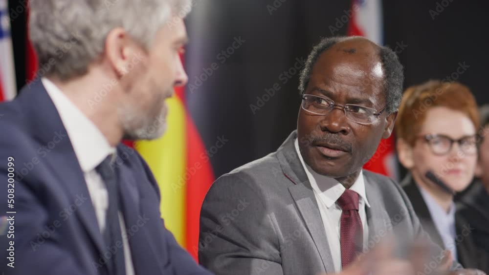 Selective focus tilt up shot of African American and Caucasian male diplomats having discussion during international press conference Selective focus tilt up shot of African American and Caucasian male diplomats having discussion during international press conference
