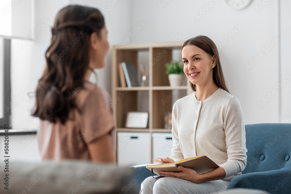 psychology, mental health and people concept - smiling psychologist with notebook and woman patient at psychotherapy session - obrazy, fototapety, plakaty 