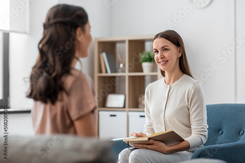 psychology, mental health and people concept - smiling psychologist with notebook and woman patient at psychotherapy session