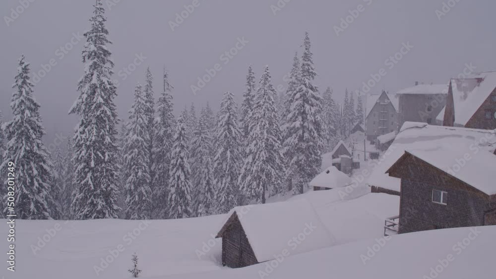 Camera pan over a village in the mountains covered in snow during a heavy snowfall Camera pan over a village in the mountains covered in snow during a heavy snowfall