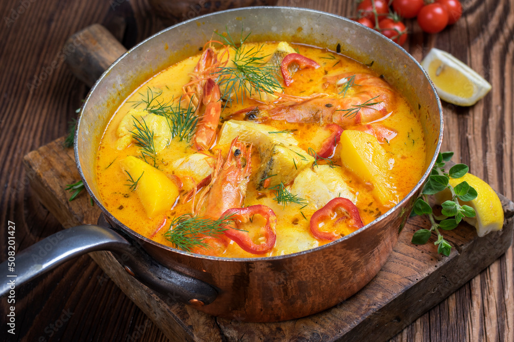 Traditional Brazilian fish soup moqueca de peixe with seafood and potatoes served as close-up in a rustic casserolle