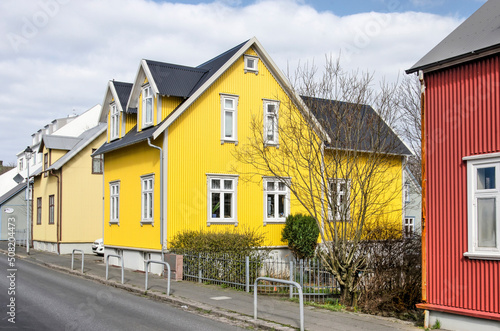 Reykjavik, Iceland, April 25, 2022: street in the old town with a traditional house with a bright yellow corrugated metal facade next to neighbours in red and pale beige