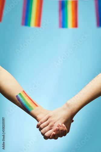 Closeup of young couple holding hands with rainbow flag in background