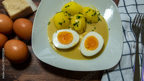 Süß saure Eier mit Petersilien Kartoffeln und Soße auf einem weißen Teller auf Holztisch mit Tuch Besteck Speck unf rohen Eiern photo