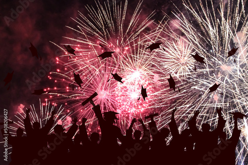 Graduation ceremony, fireworks in night sky. Silhouette of happy graduate students throwing academic square caps.