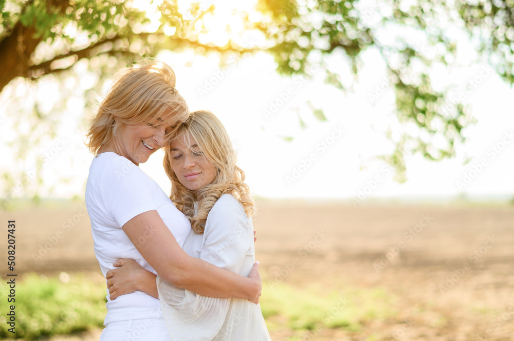Portrait of a beautiful blonde mother with her blonde daughter hugging in a field at sunset. Close up photo