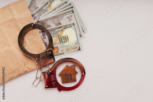 Envelope with dollars, wooden house and handcuffs on a white background. Bribe and financial fraud concept