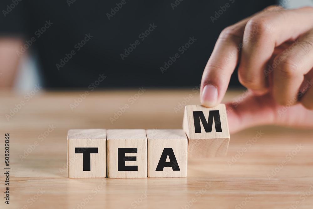Naklejka premium Man hand putting wooden cube block with TEAM text on wood table. collaboration and leadership, teamwork for brainstorming together, business concepts..