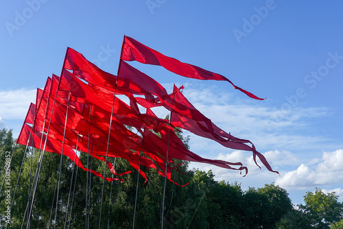 Red flags fluttering in the wind with blue sky and trees in the background