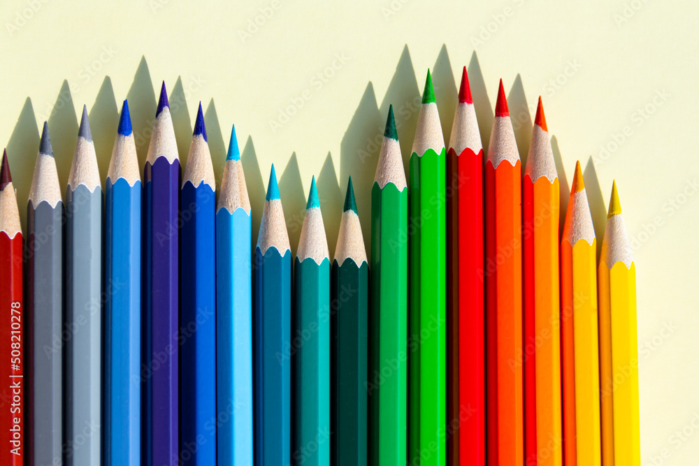 Fototapeta premium Five 5 colored pencils with wooden shavings are sharpened and lie on a light yellow background with a clear shadow from natural light on a bright, sunny day.