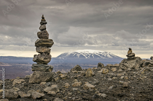 Crater rim with a tall and a lower cairn in a desolate landscape near lake Myvatn in Iceland  with a snow-capped mountain in the distance