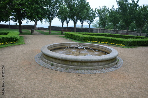 stone sandstone circular fountain in the park. built of sandstone filled with water. lined with a light threshing gravel road with a border of granite cubes, flowerbeds with orange flowers