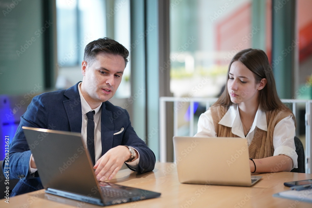 Image of young businessmen and colleague discussing document in laptop and touchpad at meeting